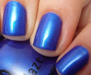 Close-up of a hand with blue metallic shimmer nail polish holding a blue bottle.