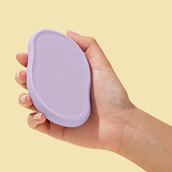 Hand holding a purple makeup sponge against a yellow background
