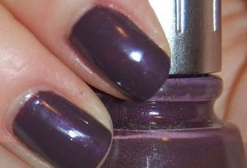 Close-up of a hand with dark purple nail polish holding a bottle of nail polish.