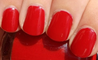 Close-up of red nail polish on a person's fingernails with a blurred background.