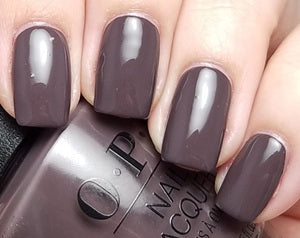 Close-up of a hand with dark nail polish holding a bottle of OPI nail polish.