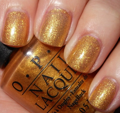 Gold glitter nail polish on nails with a bottle of O.P.I nail polish in the foreground.