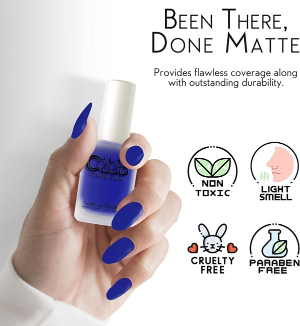 A hand with long, matte royal blue nails holds a bottle of nail polish against a clean white background. The image includes marketing text reading 'Been There, Done Matte' and feature icons for non toxic, light smell, cruelty free, and paraben free.