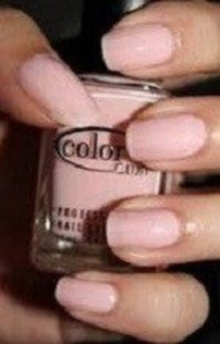 A close-up of a hand with neatly manicured nails painted in a light pink polish, holding a bottle of Color Club nail polish.