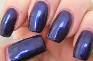 Close-up of a hand with dark blue nail polish on a neutral background