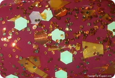 A close-up of multi-colored glitter nail polish, featuring a mix of yellow, orange, and other colors, with a clear base and small round mahogany glitter.