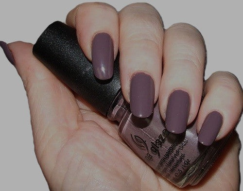 Hand holding a bottle of dark purple nail polish with matching nails.