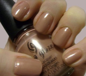 Hand holding a bottle of beige nail polish with matching nails.