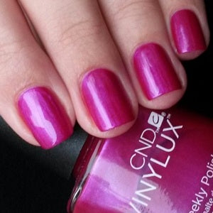 Close-up of a hand with pink nail polish holding a bottle of Vinylux nail polish.